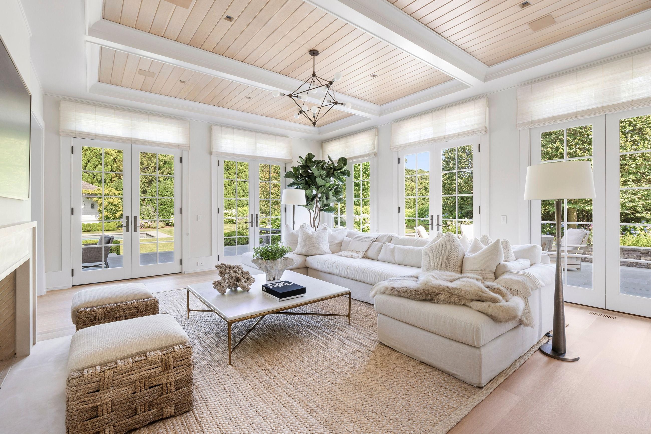 A bright, freshly cleaned living room with white sofas, a wood ceiling, and sunlight through tall French doors
