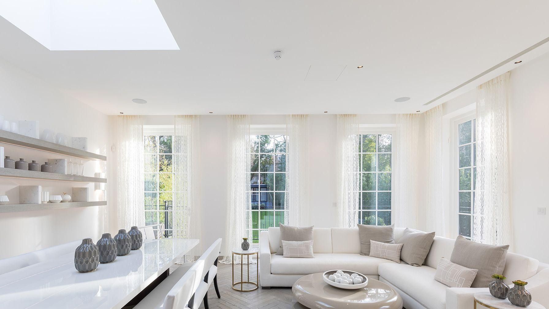 An all-white living and dining room with a skylight, sheer curtains, and tall sunlit windows