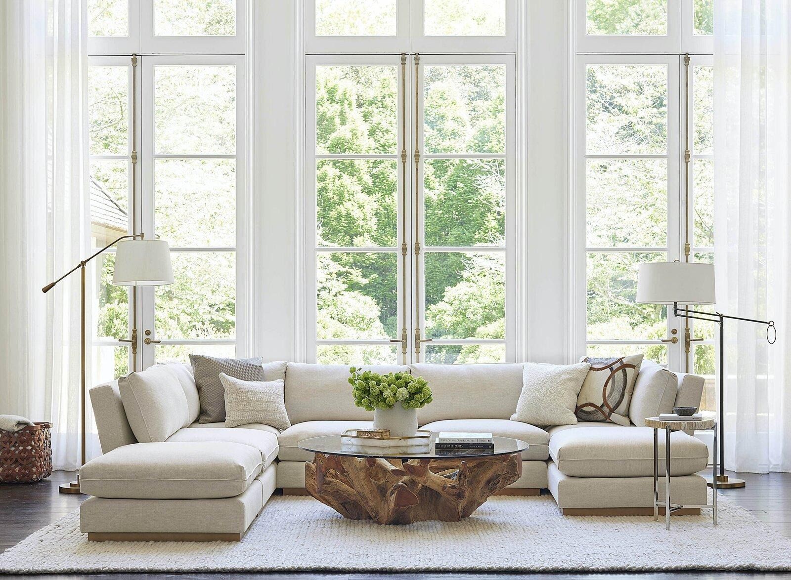 A sunlit living room with a cream sectional sofa, tall French windows, and a driftwood coffee table
